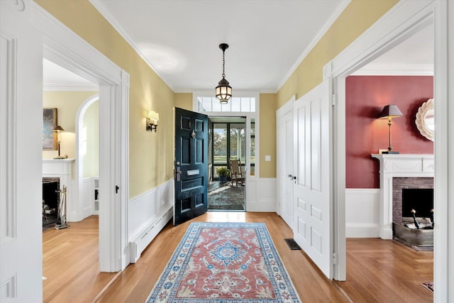 entrance foyer featuring a brick fireplace, ornamental molding, a baseboard radiator, and wood-type flooring