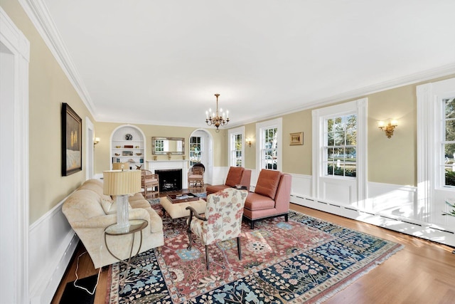 living room featuring a notable chandelier, crown molding, hardwood / wood-style flooring, baseboard heating, and built in features