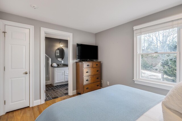 bedroom with light wood finished floors, baseboards, and ensuite bathroom