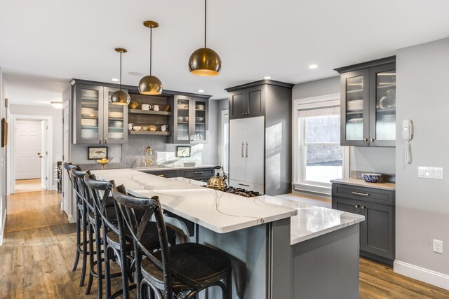 kitchen featuring light stone counters, tasteful backsplash, wood finished floors, built in refrigerator, and glass insert cabinets