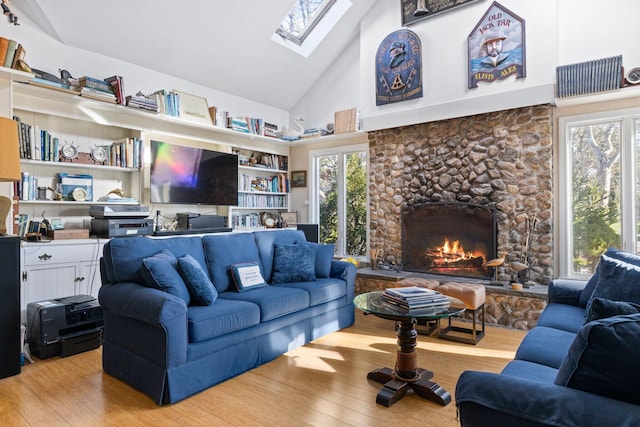 living room with a skylight, light hardwood / wood-style floors, high vaulted ceiling, and a stone fireplace