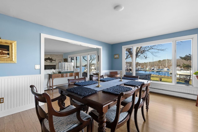 dining room featuring baseboard heating, light wood-type flooring, and a water view