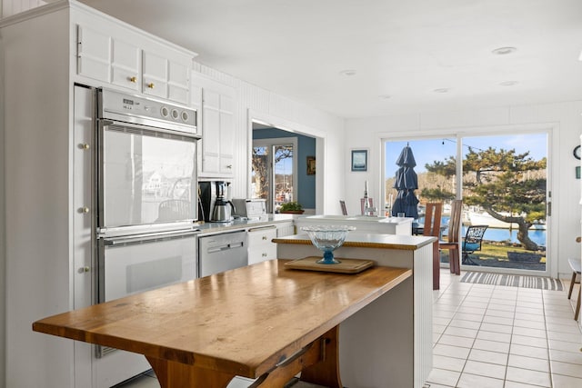 kitchen with light tile patterned floors, white cabinets, stainless steel appliances, and a healthy amount of sunlight