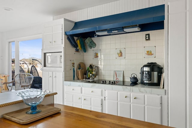 kitchen featuring white microwave, extractor fan, white cabinetry, black electric stovetop, and tasteful backsplash