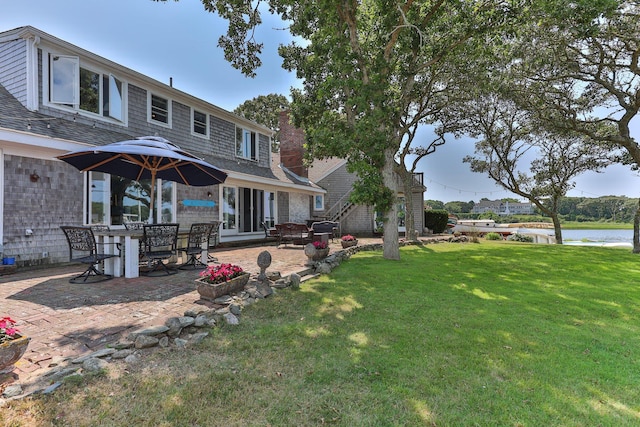 rear view of property with a yard, a water view, and a patio