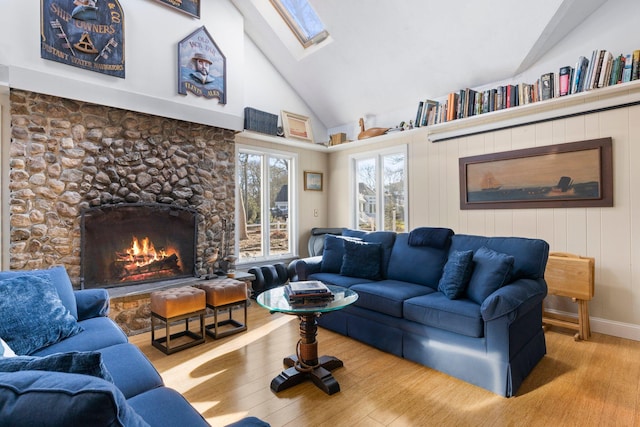 living room featuring light hardwood / wood-style floors, high vaulted ceiling, a skylight, and a stone fireplace