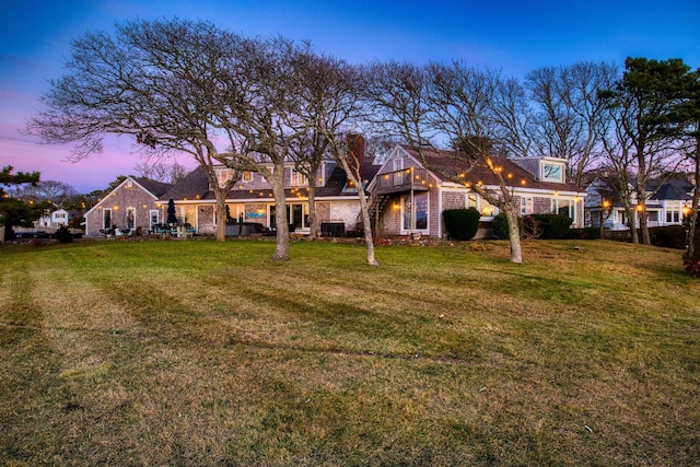back house at dusk featuring a lawn