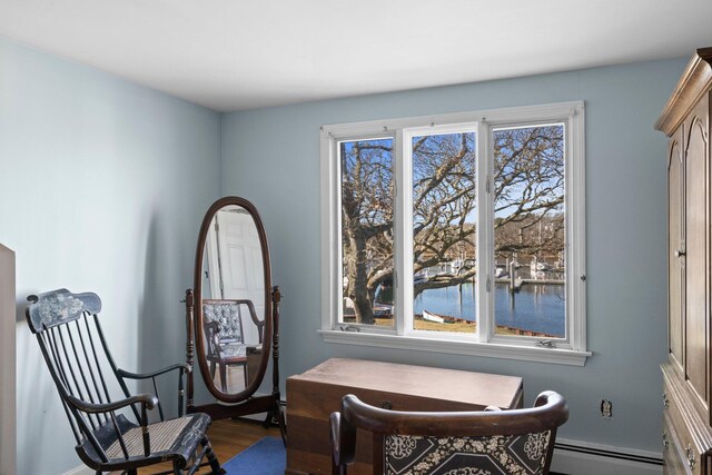sitting room featuring a water view, a baseboard heating unit, and hardwood / wood-style floors