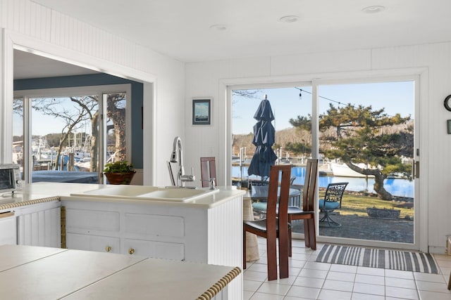 kitchen with sink, light tile patterned flooring, white cabinets, and a water view