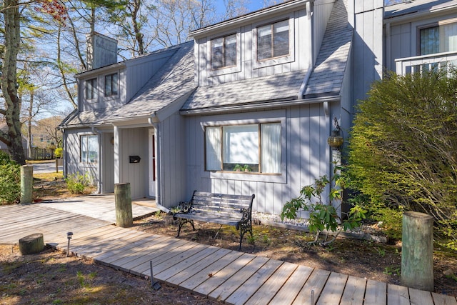 view of front of house with a shingled roof, a wooden deck, and a chimney
