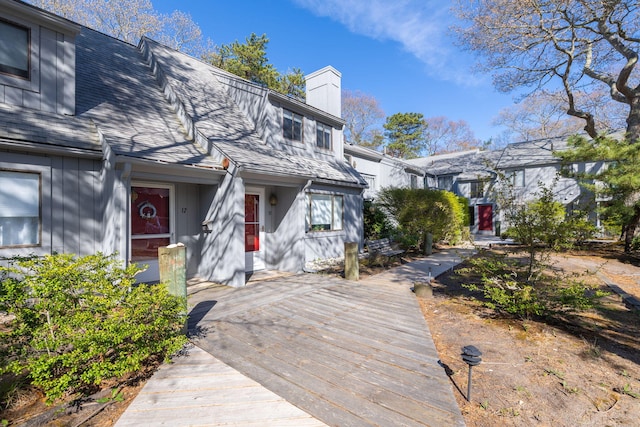 view of front of home featuring board and batten siding, a chimney, a shingled roof, and a wooden deck