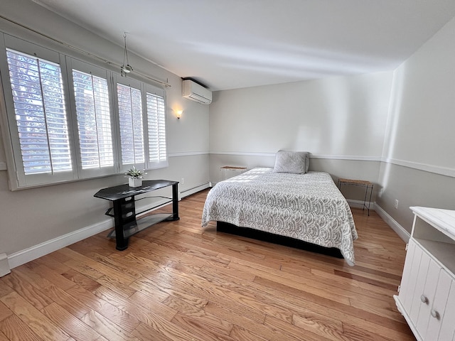 bedroom featuring baseboard heating, light hardwood / wood-style floors, and a wall mounted air conditioner