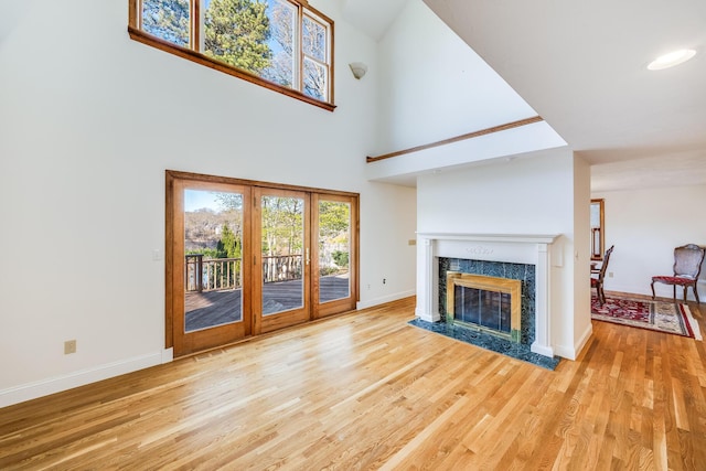 unfurnished living room featuring baseboards, a high ceiling, a tile fireplace, and wood finished floors
