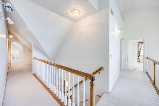 hallway featuring an upstairs landing, visible vents, carpet floors, and vaulted ceiling