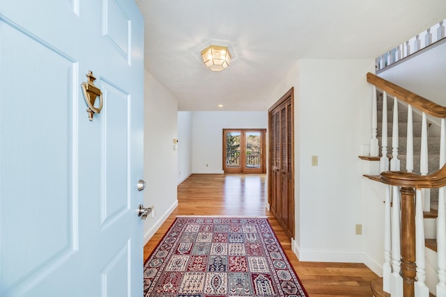 foyer with baseboards, light wood finished floors, and stairway