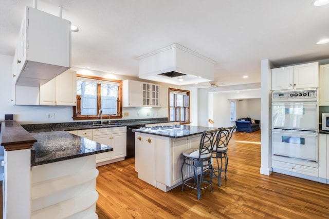 kitchen featuring double oven, a kitchen breakfast bar, a sink, light wood finished floors, and dishwasher
