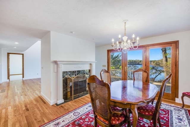 dining space featuring baseboards, an inviting chandelier, a water view, a fireplace, and light wood-type flooring