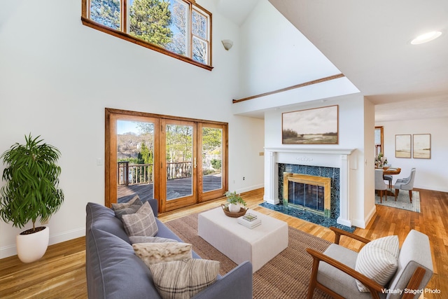 living area featuring baseboards, a fireplace, a towering ceiling, and wood finished floors