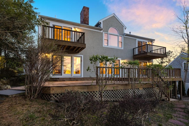 back of property at dusk with a balcony and a chimney