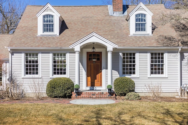 cape cod house with a shingled roof, a front yard, and a chimney