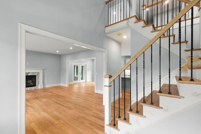 stairway with a high ceiling, hardwood / wood-style floors, a high end fireplace, and french doors