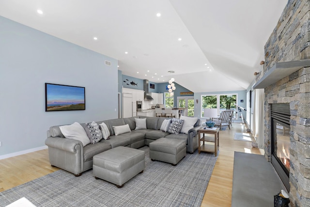 living area featuring light wood finished floors, baseboards, visible vents, vaulted ceiling, and a stone fireplace