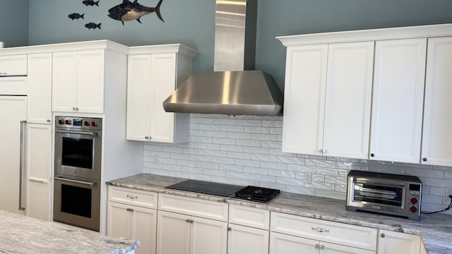 kitchen featuring black electric stovetop, wall chimney range hood, stainless steel double oven, and decorative backsplash