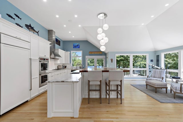 kitchen featuring a kitchen island with sink, stainless steel double oven, a wealth of natural light, and white cabinets