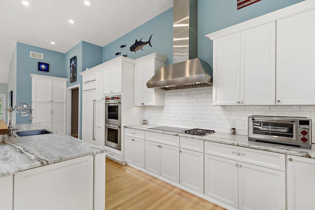 kitchen with tasteful backsplash, visible vents, double oven, a sink, and wall chimney exhaust hood