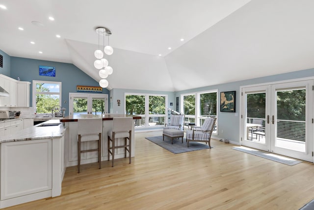 kitchen with light wood finished floors, white cabinets, decorative light fixtures, vaulted ceiling, and french doors