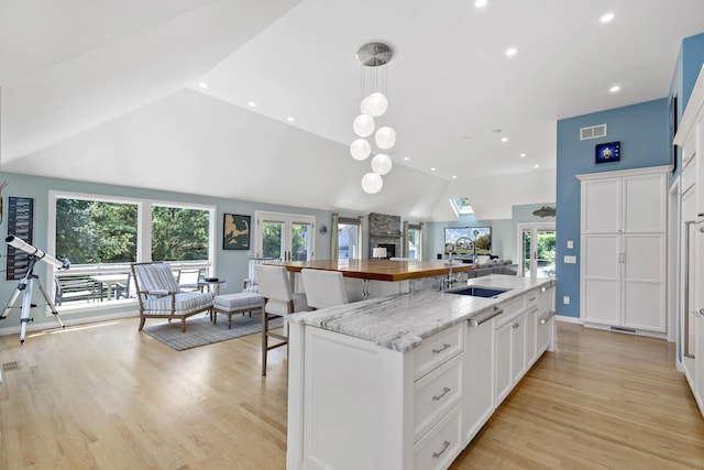 kitchen with lofted ceiling, plenty of natural light, a kitchen island with sink, and white cabinets