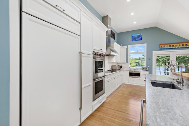 kitchen featuring decorative backsplash, stainless steel double oven, white cabinets, a sink, and light wood-type flooring