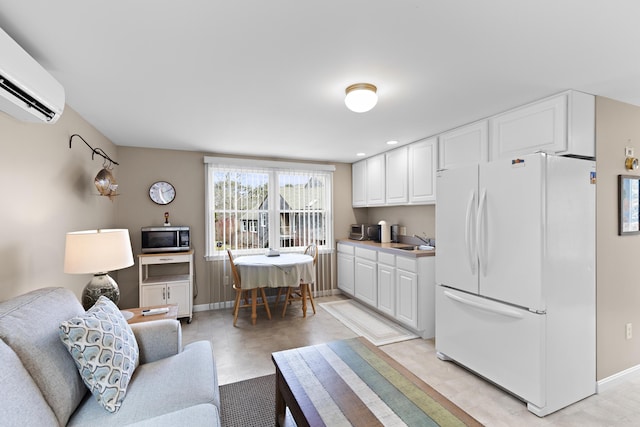 kitchen featuring a wall unit AC, a sink, white cabinets, freestanding refrigerator, and stainless steel microwave