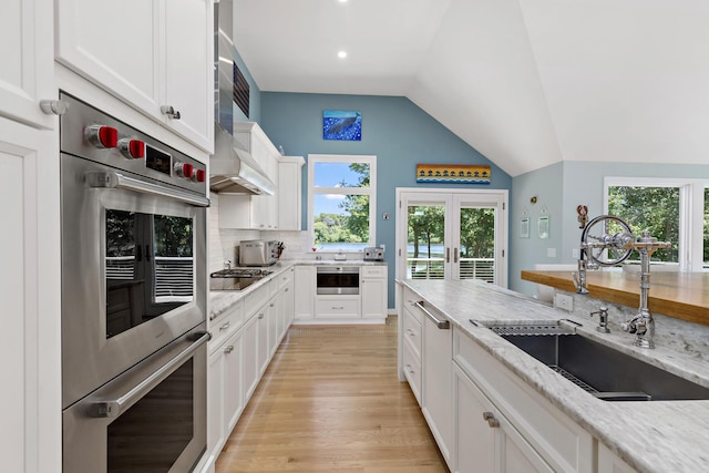 kitchen featuring double oven, a sink, white cabinetry, vaulted ceiling, and tasteful backsplash