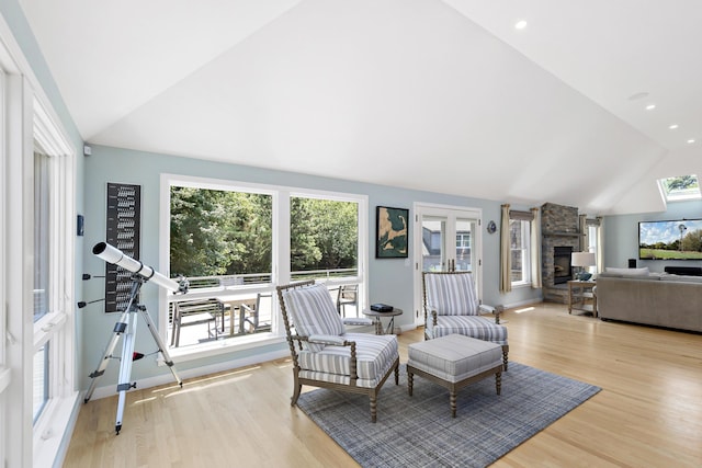 living area featuring recessed lighting, vaulted ceiling, a stone fireplace, light wood-type flooring, and baseboards