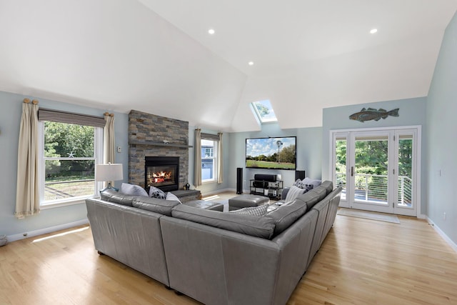 living area featuring high vaulted ceiling, light wood-type flooring, a healthy amount of sunlight, and a fireplace