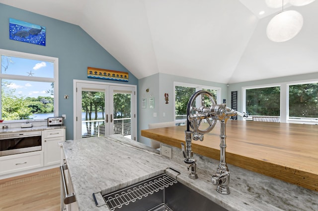 interior space with french doors, lofted ceiling, white cabinetry, light stone countertops, and light wood-type flooring