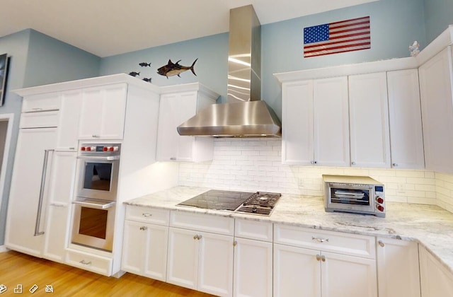 kitchen with black stovetop, tasteful backsplash, double oven, white cabinetry, and wall chimney exhaust hood