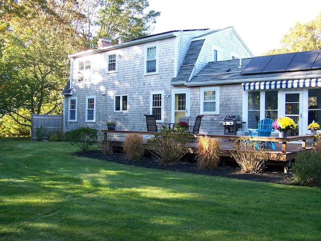 back of property featuring a gambrel roof, a lawn, roof mounted solar panels, a wooden deck, and a chimney