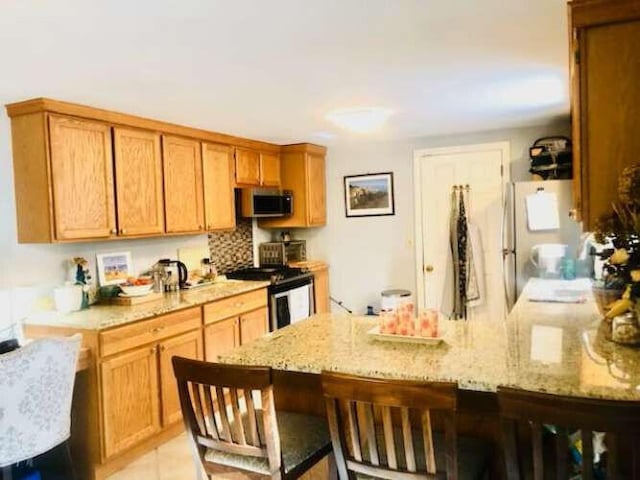 5 Greyhampton Rd, West Yarmouth, MA 02673 - kitchen with appliances with stainless steel finishes, a peninsula, a breakfast bar, light stone countertops, and brown cabinetry
