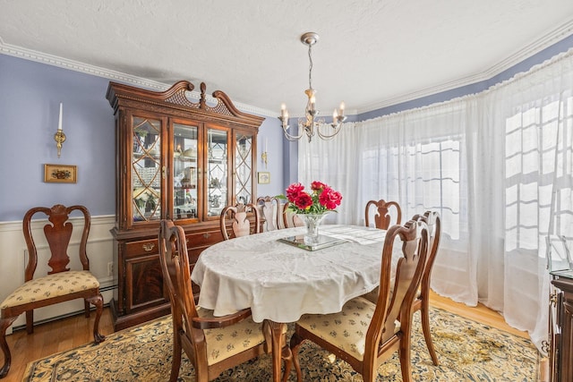 dining area with light wood-style floors, a chandelier, crown molding, and a textured ceiling