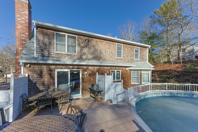 rear view of house featuring outdoor dining space, a chimney, and a wooden deck