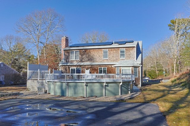 back of house featuring a chimney, a lawn, a deck, and solar panels