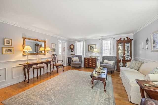 living area with a decorative wall, wainscoting, wood finished floors, and crown molding