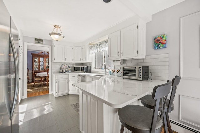 kitchen with a toaster, stainless steel appliances, a peninsula, white cabinets, and backsplash