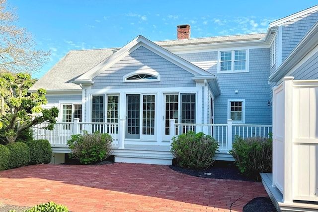 rear view of property with a chimney and roof with shingles