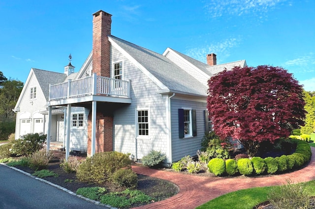 view of property exterior with a shingled roof, a chimney, and a balcony