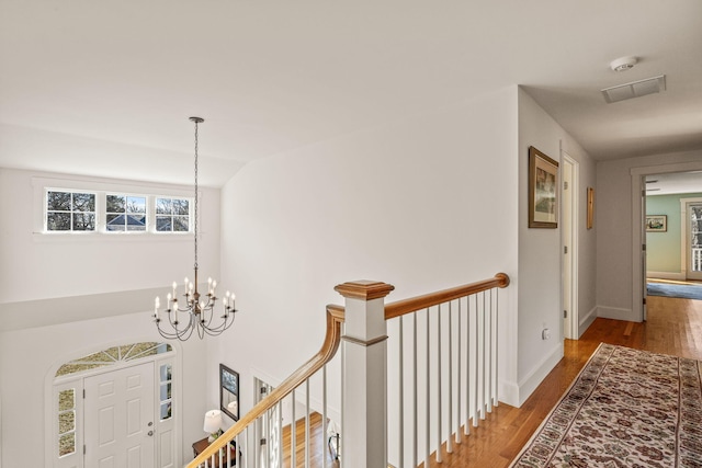 hall featuring an upstairs landing, wood finished floors, a chandelier, and baseboards