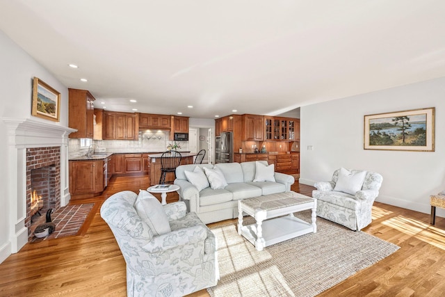 living room with a tile fireplace, sink, and light hardwood / wood-style flooring