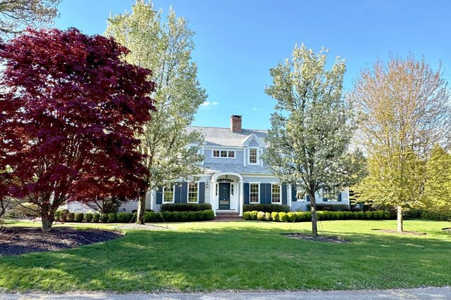 shingle-style home featuring a chimney and a front yard